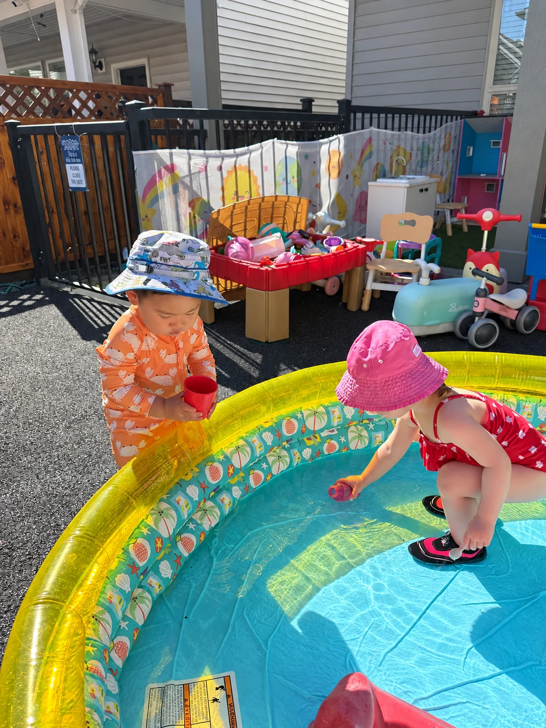 Two children exploring water with cups in the outdoor play area